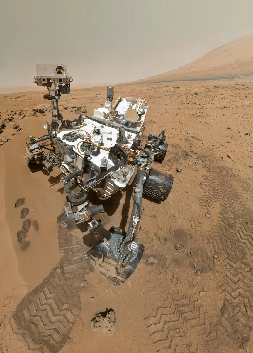 Le rover Curiosity sur le sol martien, devant des reliefs du cratère Gale.
