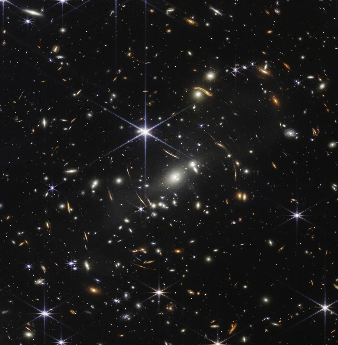 Champ profond de James Webb montrant des galaxies, des arcs lumineux et des étoiles au premier plan.