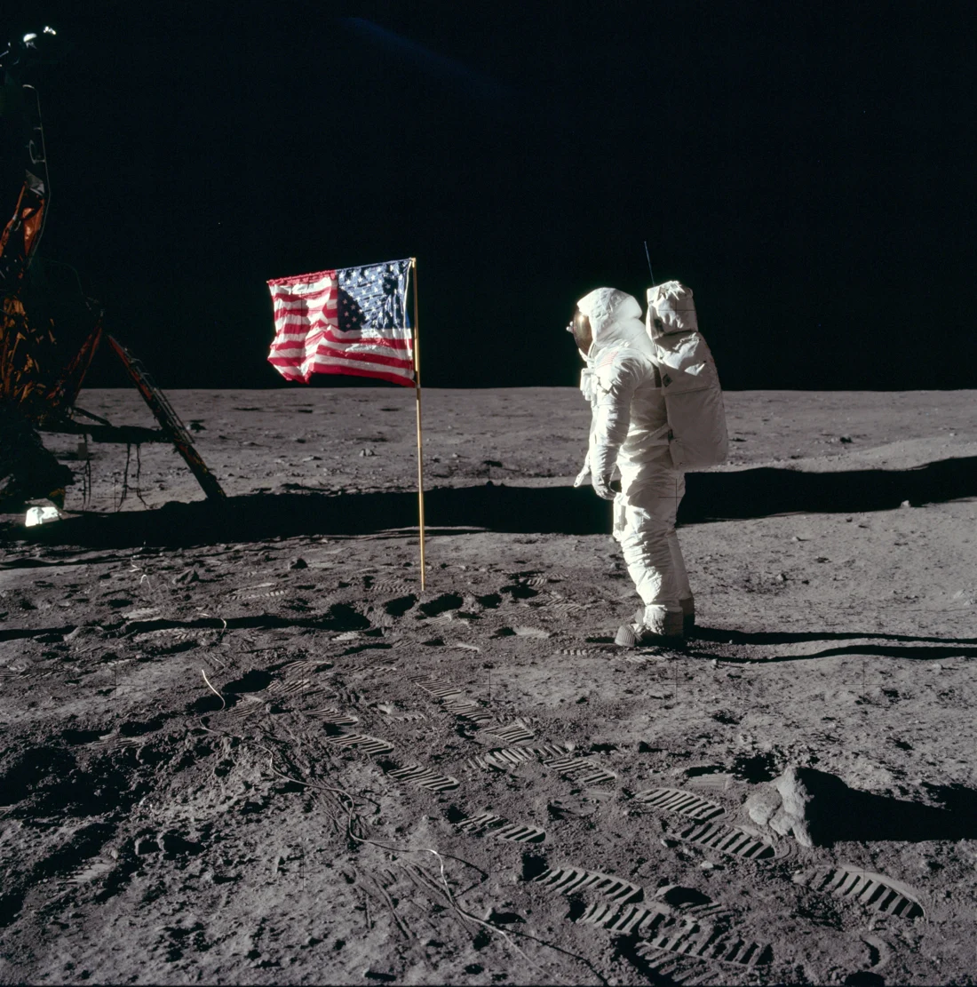 Buzz Aldrin en combinaison spatiale salue le drapeau américain sur le sol lunaire.